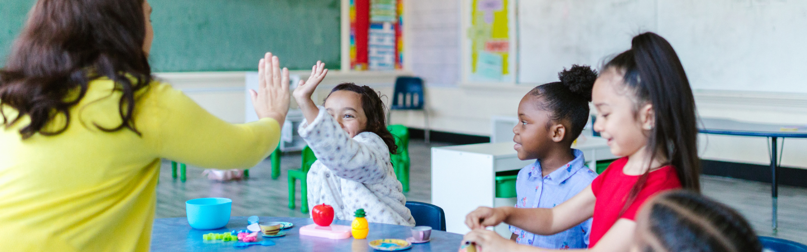 Teacher high-fiving a young student in a classroom next to her peers