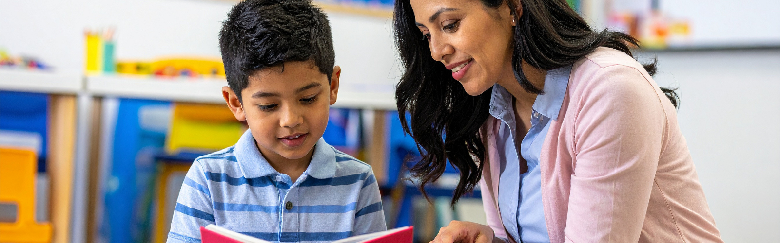 Young student with his teacher learning to read in the classroom