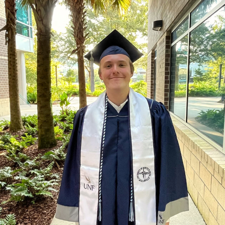 THRIVE student in UNF regalia smiling outside on UNF campus