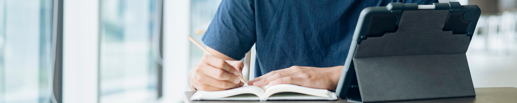 student writing in notebook and iPad