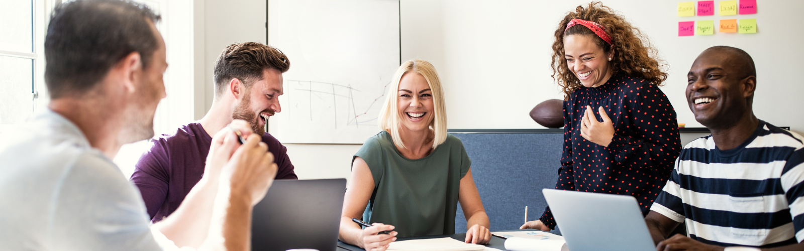 Five professionals grouped at a table working on a project smiling