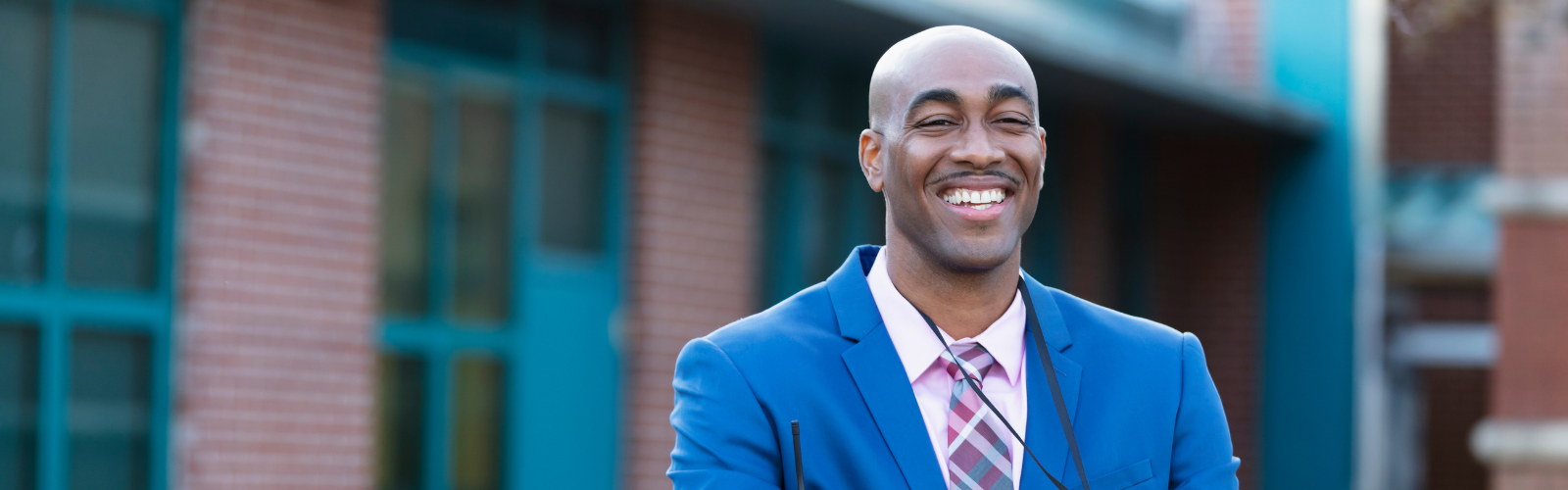 A principal smiles while standing outside a school. 