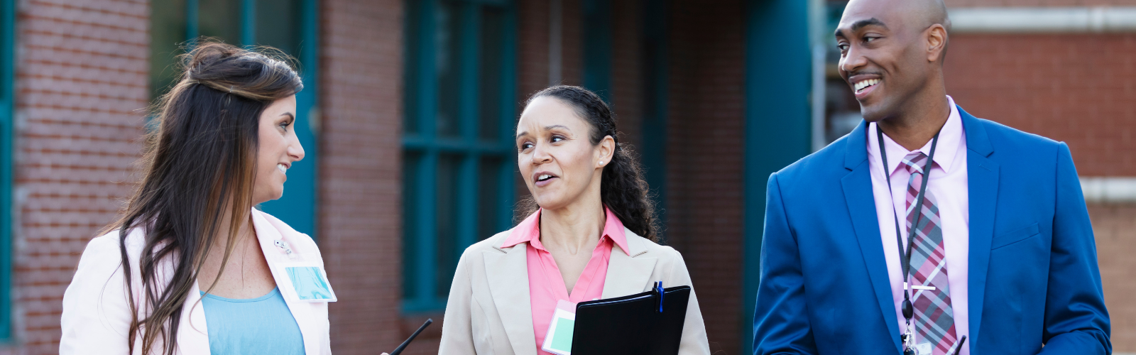 Three educational professionals communicating while walking outdoors in professional clothes
