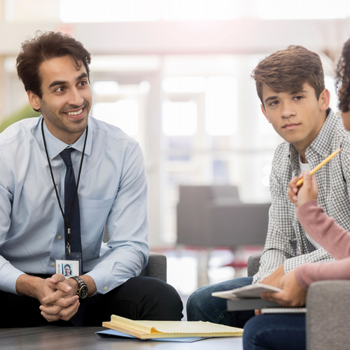 Male education professional sitting, smiling and conversing with two students 