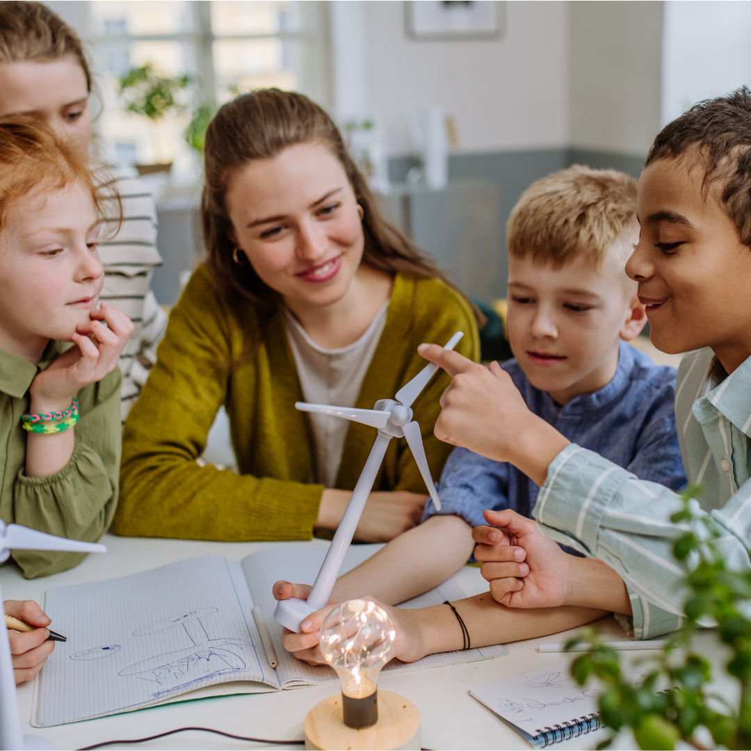 A science teacher sits at a table surrounded by students working on miniature wind turbines. 