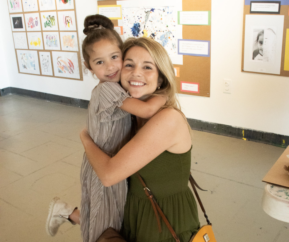 Teacher and student embrace at art exhibit. 