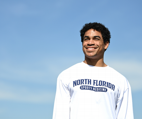 UNF student smiling in white UNF t-shirt with blue sky