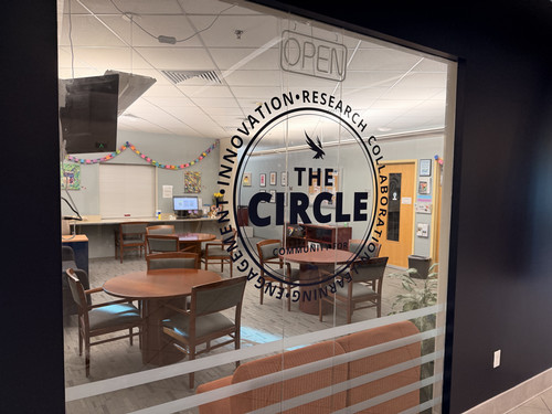 Glass window with THE CIRCLE logo looking into a community room