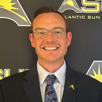 Jeff Bacon in a suit and blue tie smiling with glasses on