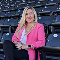 Kristi Dosh in a pink blazer sitting on navy bleachers smiling