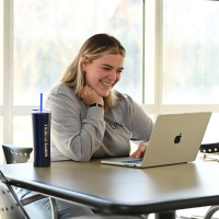 A UNF student on her computer smiling 