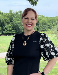 Janice Woods wearing a black top standing outside with trees in the background.