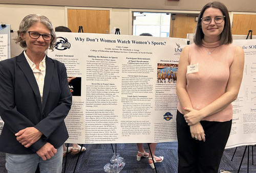 Two women stand by a research poster on women’s sports viewership.