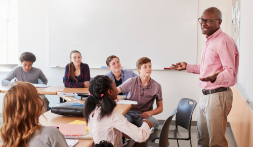 A male teacher in a classroom speaking to a group of engaged students