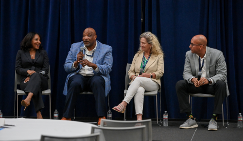 A group of four panelists holding microphones on stage at the Silverfield Coaching Symposium 