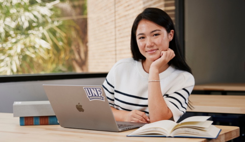 UNF student smiling at the camera in a modern workspace on her computer