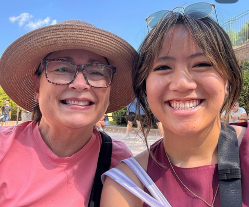 Two women smiling outdoors, one wearing a sunhat and glasses