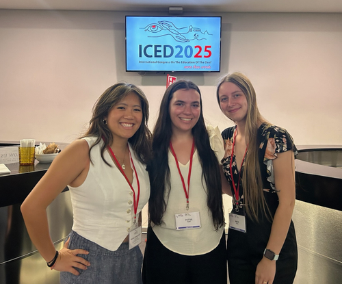 Three women pose at ICED 2025 conference with even sign behind