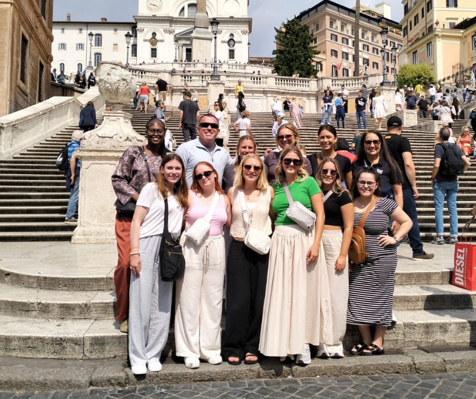 A group of students and faculty stand together on steps in Italy.