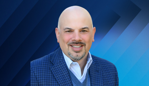 Mike Vitti headshot with a blue geometric background.