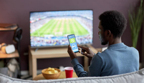 Image of person on couch with phone sports gambling in front of TV