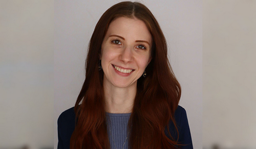 Smiling woman with long auburn hair in a studio headshot against a light gray background.