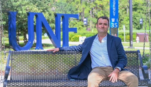Xavier Rozas sitting on a swing smiling on the UNF campus