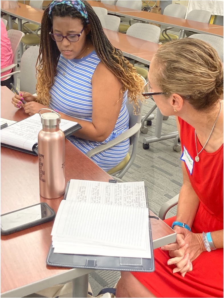 Two women discuss notes during a writing-focused session.