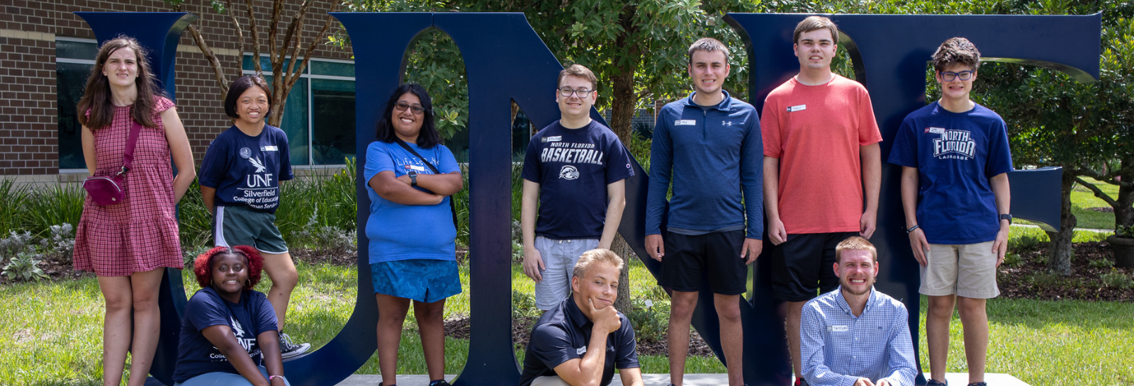 USoar students posing in front of the UNF sign. Some are sitting while others are standing.
