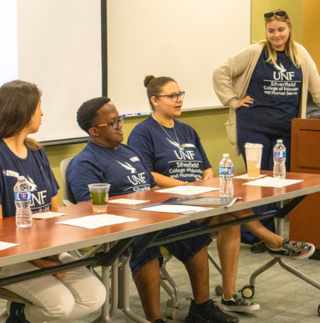 USoar students participating in a panel and wearing UNF Silverfield College t-shirts