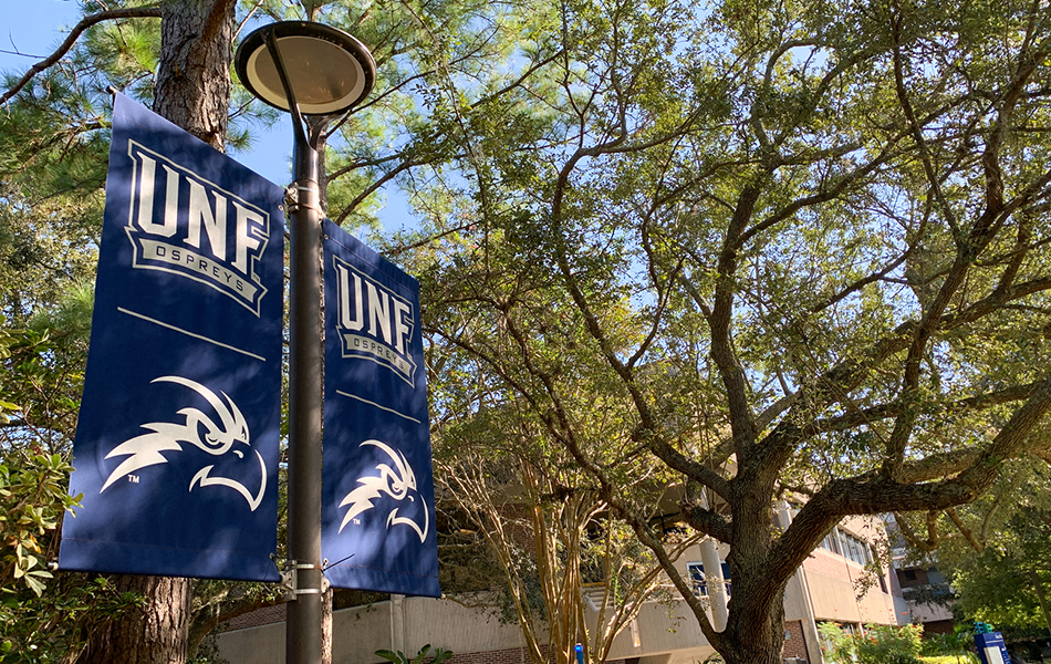 UNF banners with an osprey logo on a light post in front of a building and trees