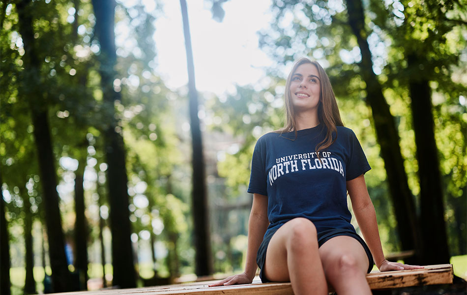 Girl in unf shirt smiling while sitting on an outdoor picnic table