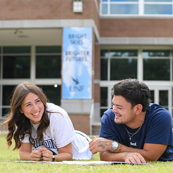 2 students smiling while sitting on the lawn