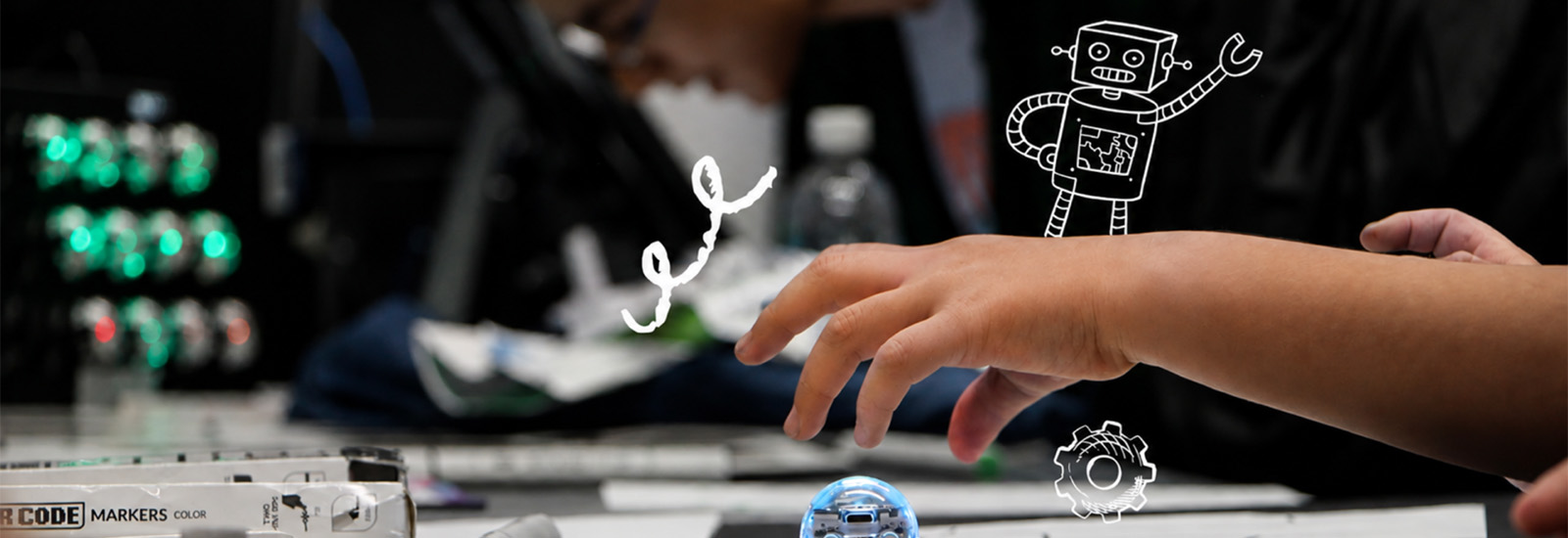 a child's hand above some electronics on a table with stencil drawings of a robot and a gear