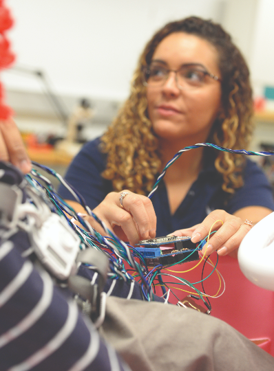 Female UNF student in an engineering lab connecting wires to a piece of technology