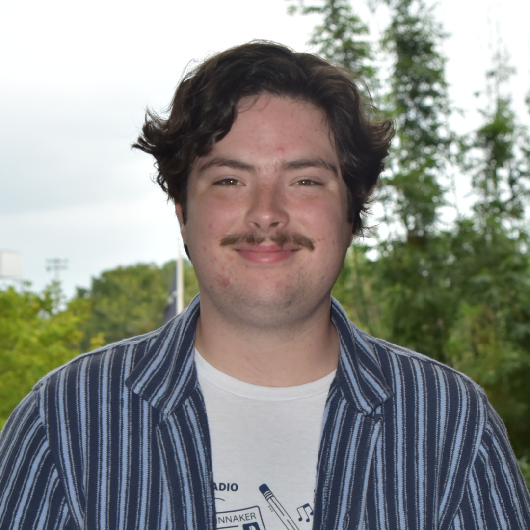 Aidan is standing outside in a blue and white striped shirt.