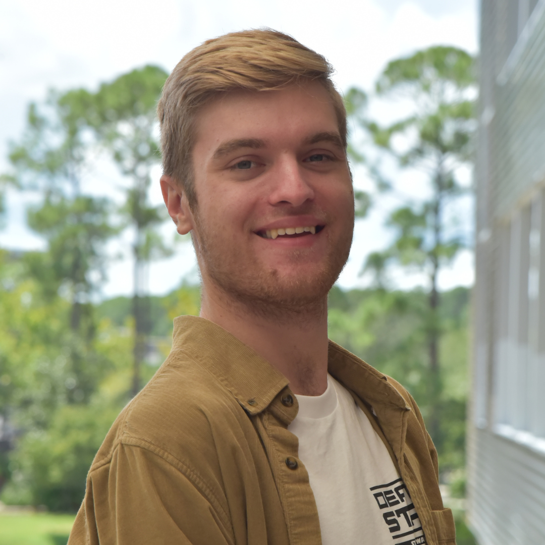 Austin is wearing a tan shacket and smiling