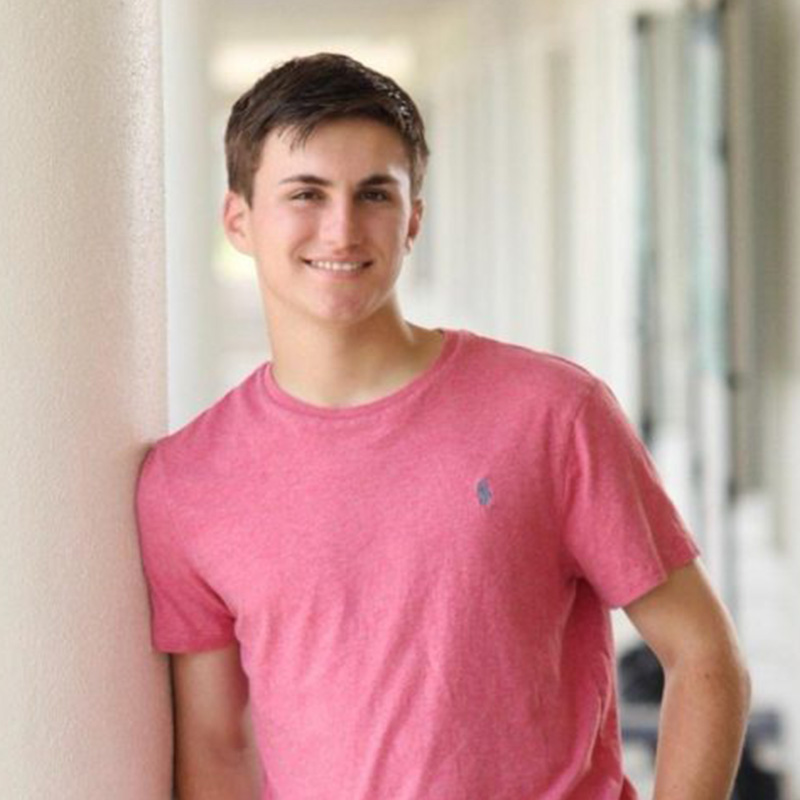 David in a bright pink shirt leaning against a white column