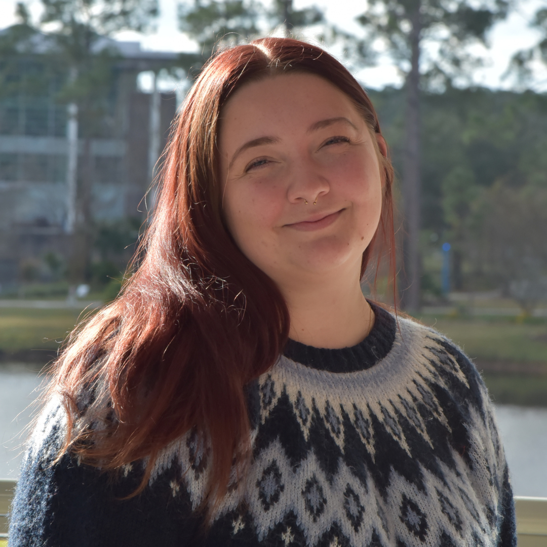 Emma has long red hair and is wearing a sweater