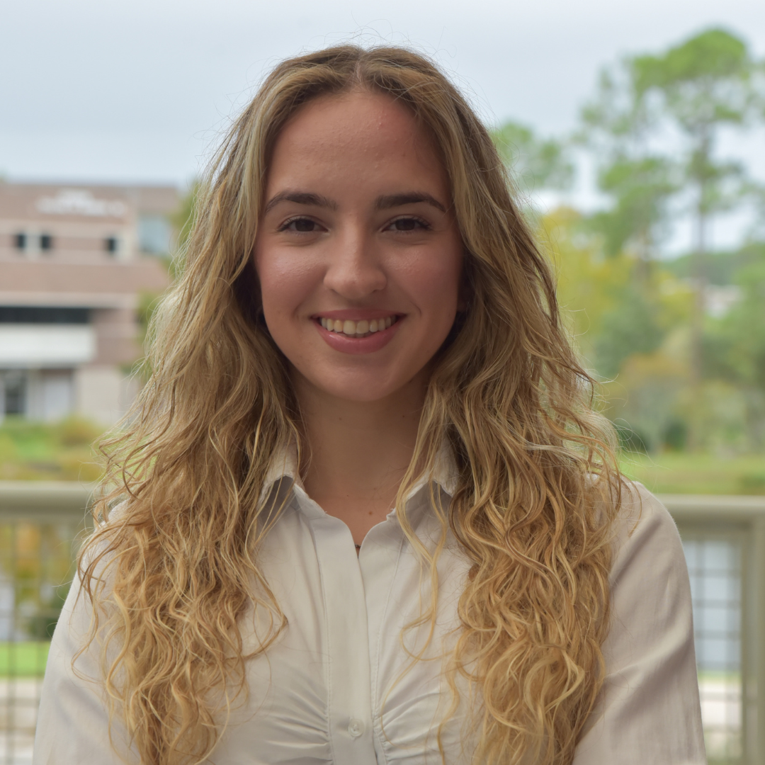 Ester has long blonde hair and she is standing outside in a white shirt.