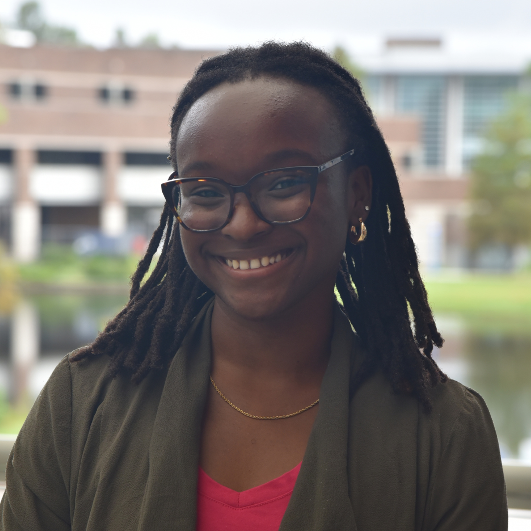 Gabrielle is wearing a red shirt and black jacket and is smiling.
