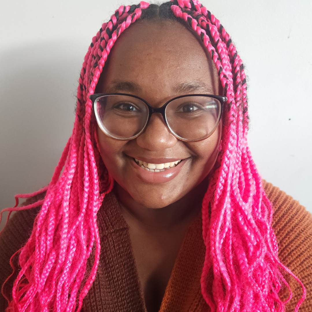 Kiela with pink braids and black glasses standing in front of a white background
