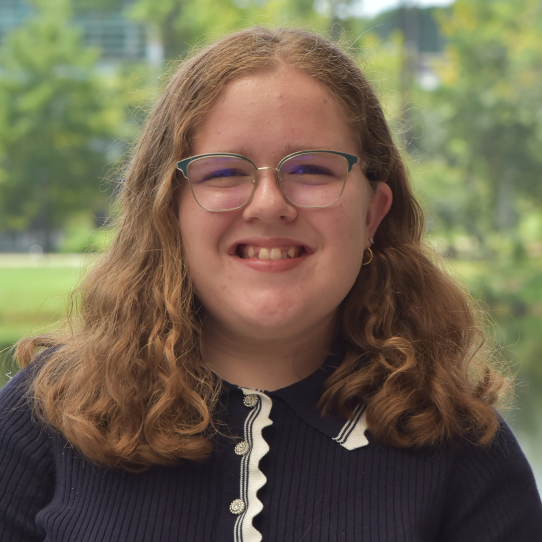 Madeline has blonde hair and is wearing a navy blue shirt. 