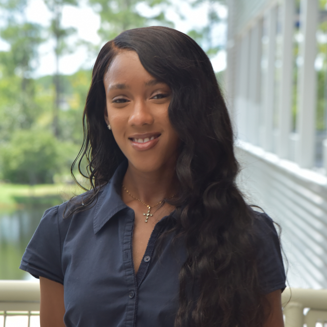 Mya is wearing a black shirt and standing outside
