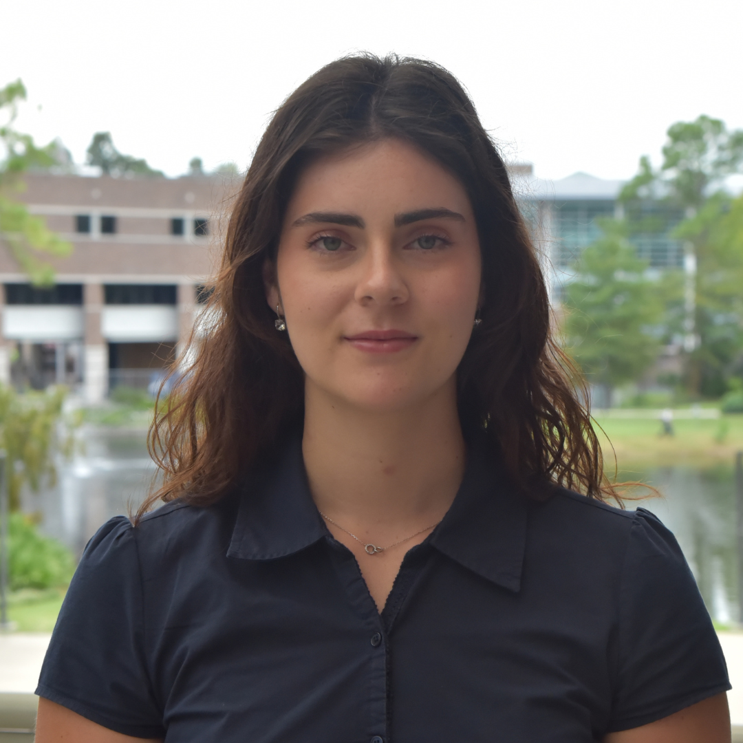 Raquel has dark hair and is wearing a blue shirt.