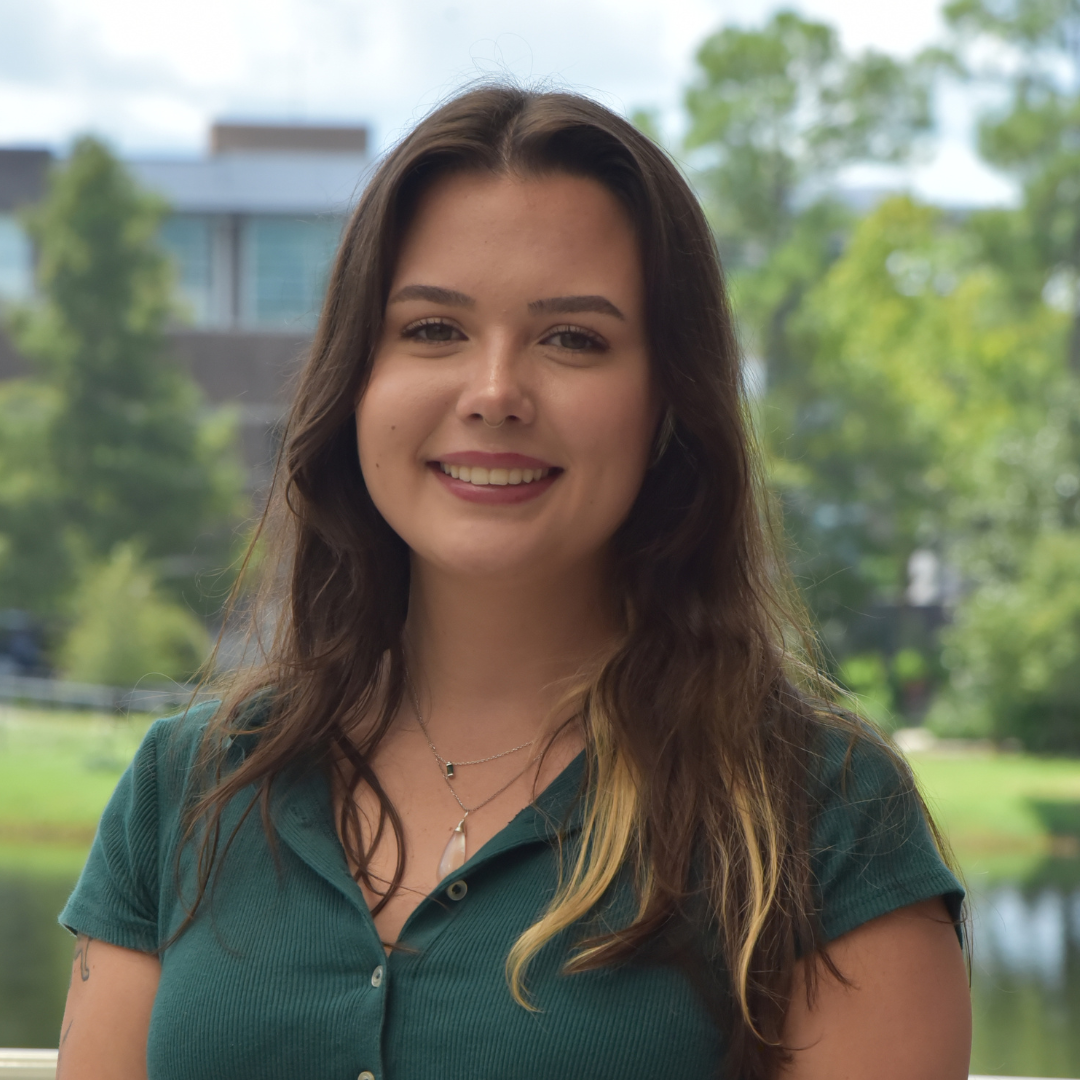 Sasha is wearing a green shirt and standing outside.