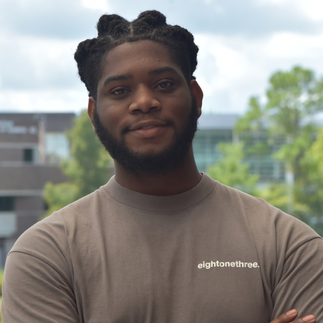 Tashaun is standing outside in a tan t-shirt. 