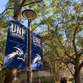 UNF banner on a lamp post surrounded by trees