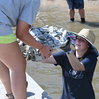 Student conducting field research in river handing coral to other student