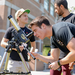 Students on the green with one looking through a telescope